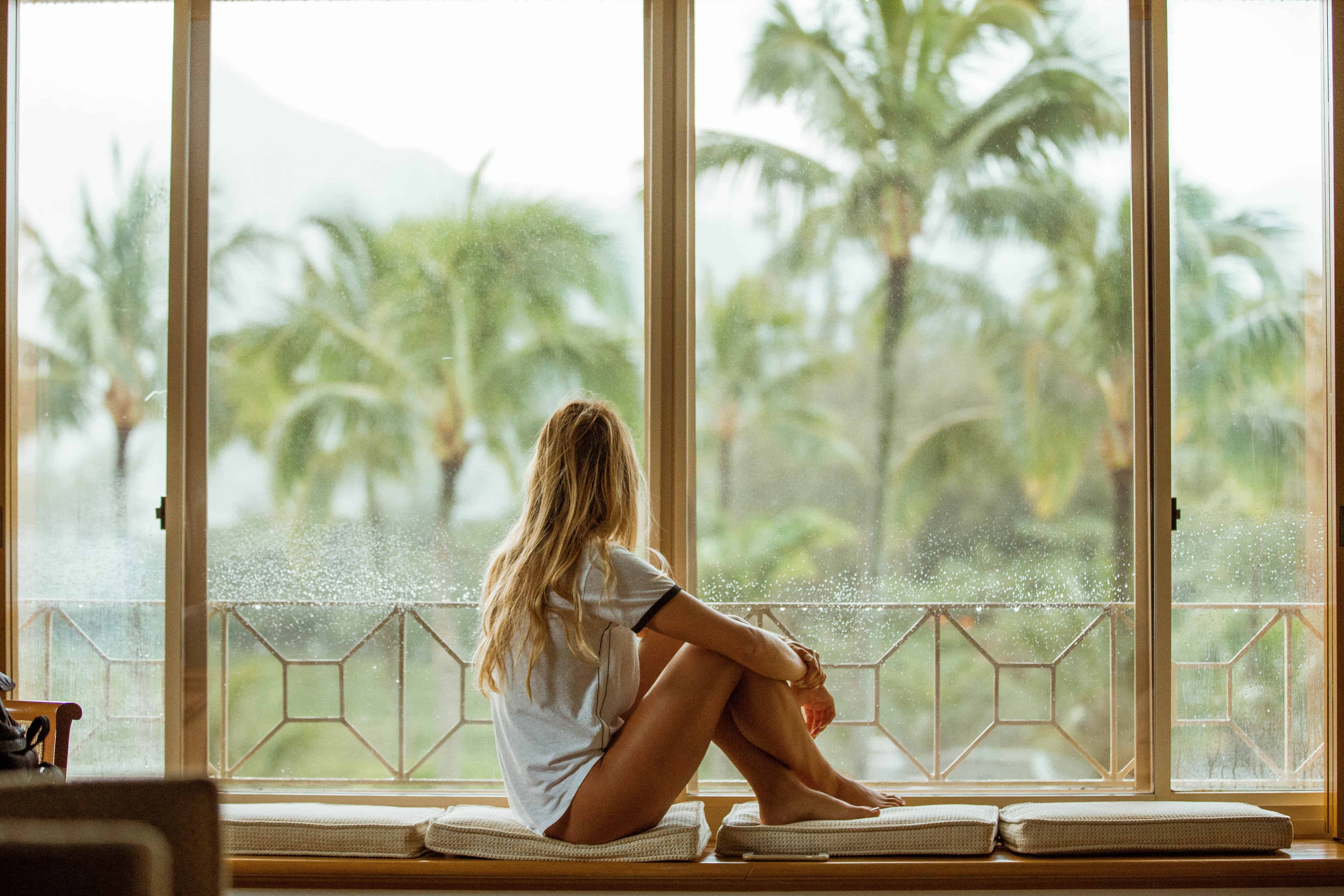 woman looking out windows with palm trees in the distance