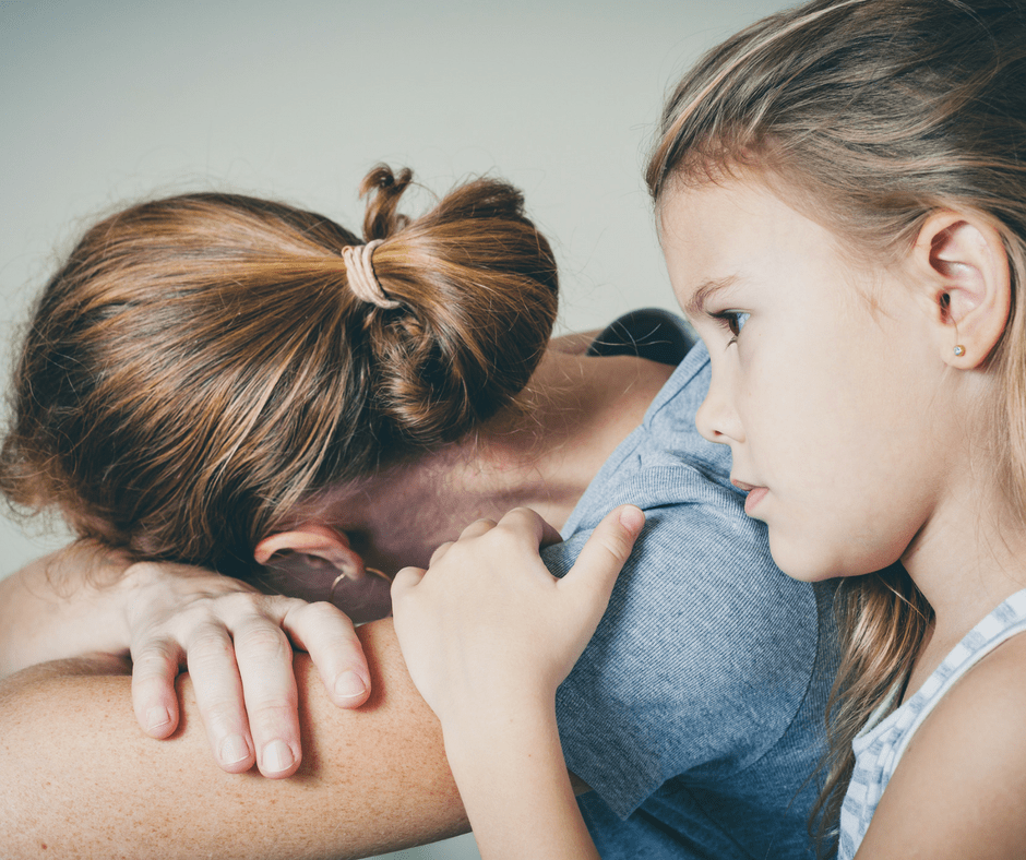 mother with head down in her arms while daughter consoles her