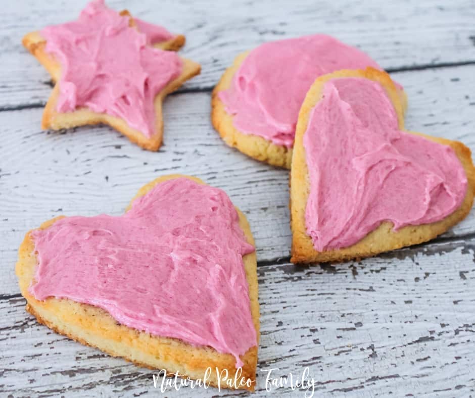four pink frosted heart shaped cookies on white wood