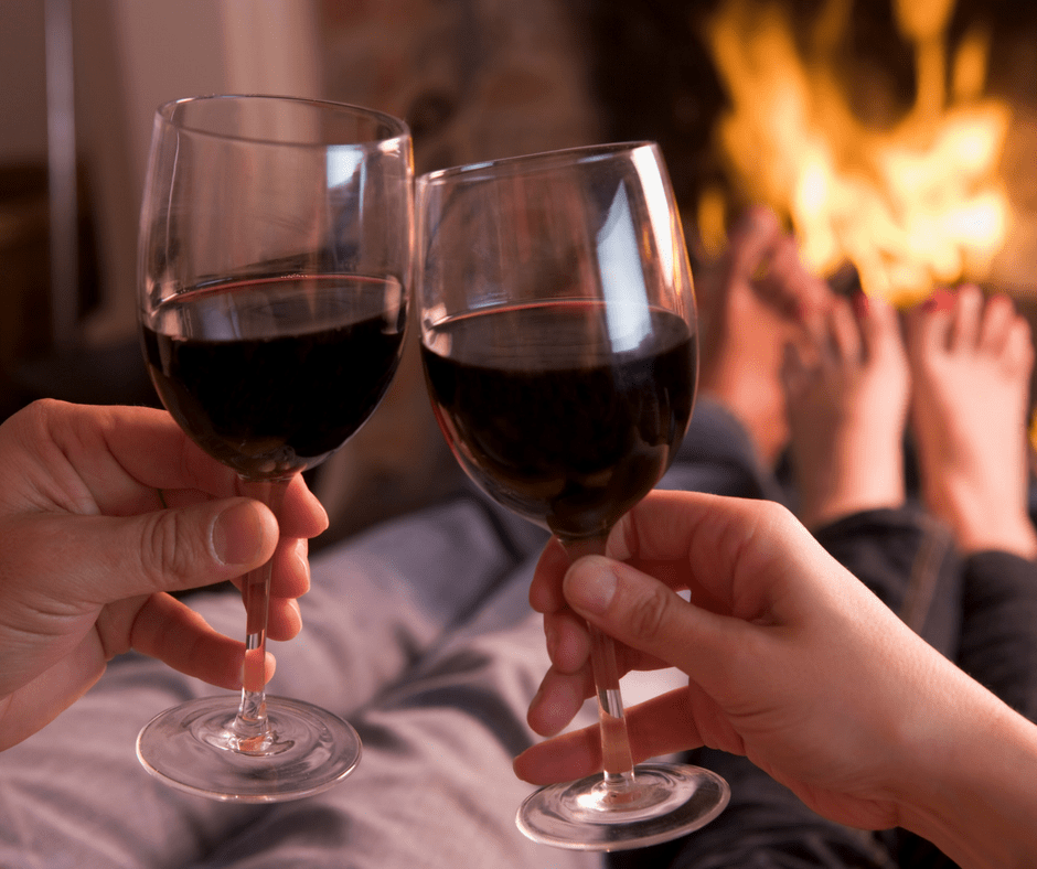 man and woman clinking wine glasses in front of a fire